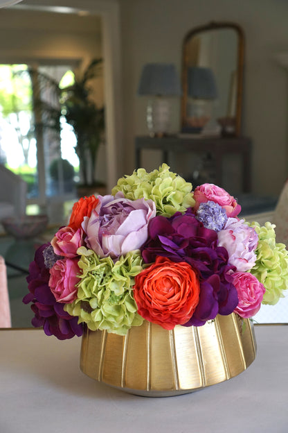 A beautiful centerpiece of bright and colorful faux flowers including green hydrangea, pink roses, and other orange and purple blossoms.