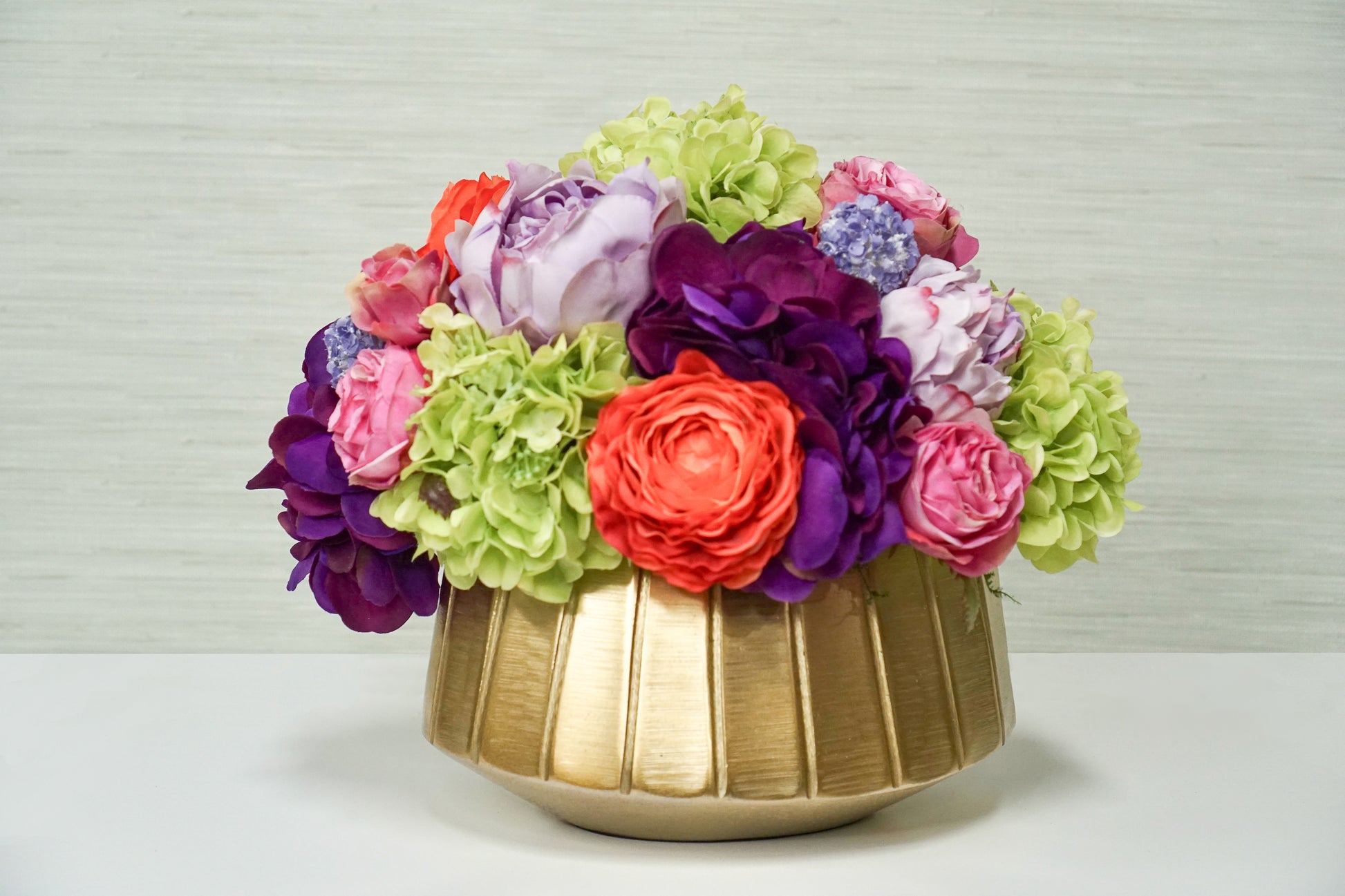 A beautiful centerpiece of bright and colorful faux flowers including green hydrangea, pink roses, and other orange and purple blossoms.