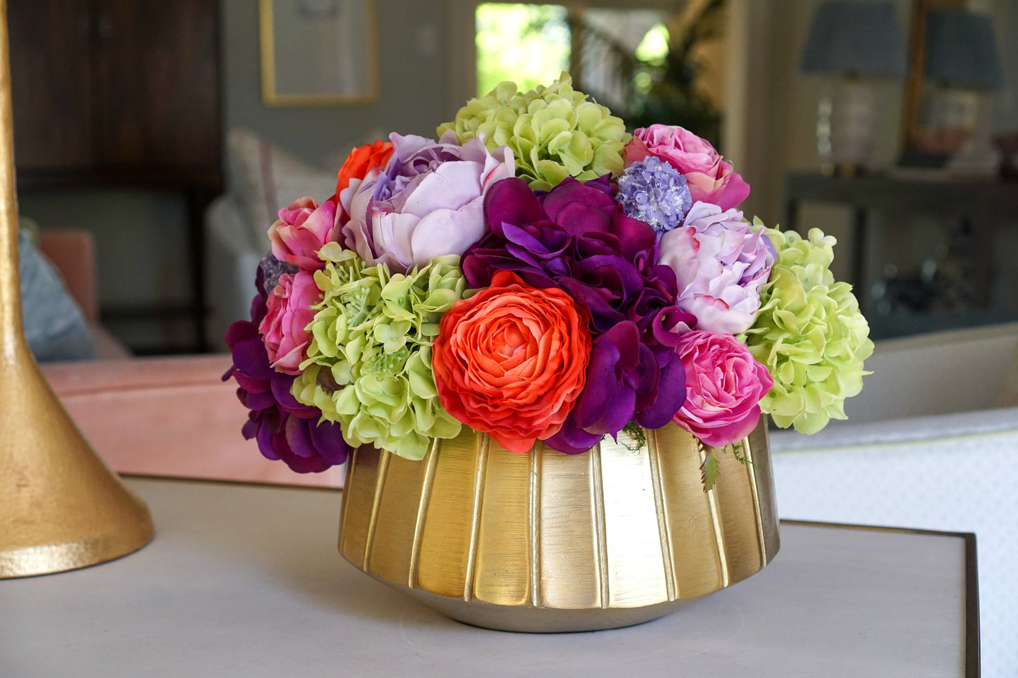 A beautiful centerpiece of bright and colorful faux flowers including green hydrangea, pink roses, and other orange and purple blossoms.