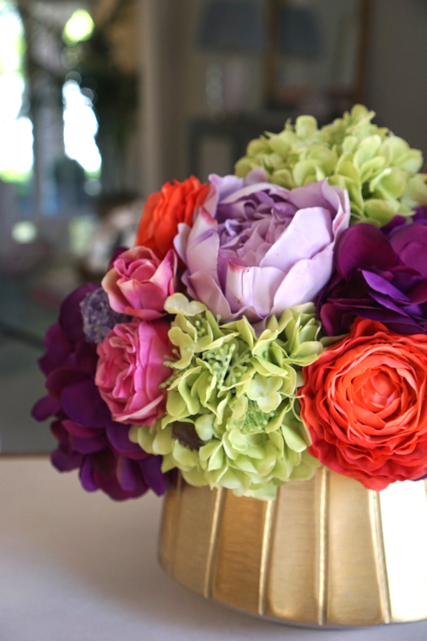 A beautiful centerpiece of bright and colorful faux flowers including green hydrangea, pink roses, and other orange and purple blossoms.