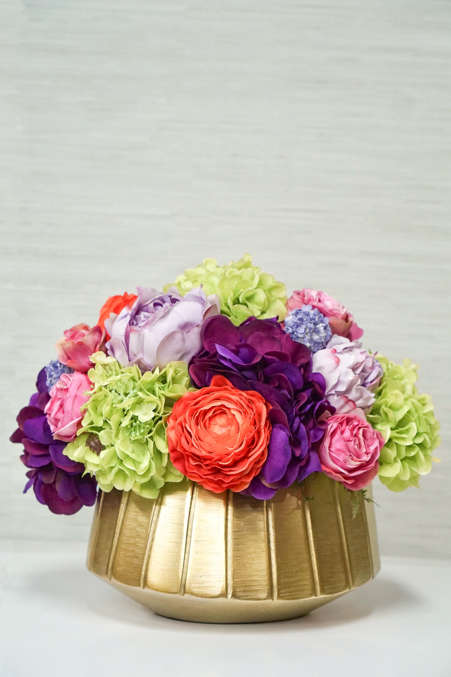 A beautiful centerpiece of bright and colorful faux flowers including green hydrangea, pink roses, and other orange and purple blossoms.