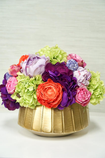 A beautiful centerpiece of bright and colorful faux flowers including green hydrangea, pink roses, and other orange and purple blossoms.